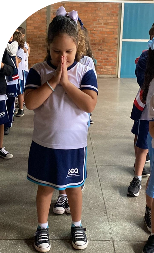 Aluna da Educação Infantil com as mãos juntas no pátio da escola