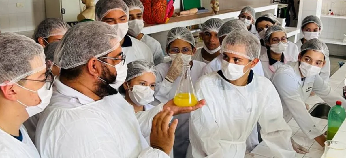 Alunos de jaleco e touca em uma aula prática de laboratório